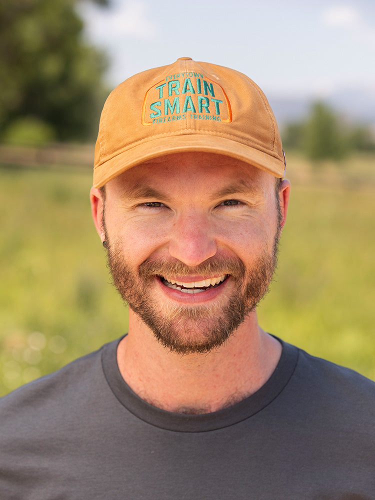 Front view of man wearing light brown Carhartt canvas baseball cap with embroided orange and teal logo that reads: TRAIN SMART Everytown Firearms Training.
