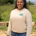 Front view of woman wearing a khaki-colored long sleeve unisex shirt with a teal and orange logo on left chest that reads: TRAIN SMART Everytown Firearms Training.
