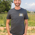 Front view of a man wearing a gray short sleeve unisex t-shirt with a small orange and white logo on left chest that reads: TRAIN SMART Everytown Firearms Training.