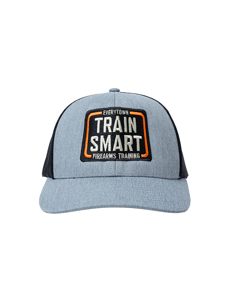 Front view of gray trucker hat with black mesh in the back. Embroided orange, white, and black logo on front of hat reads: TRAIN SMART Everytown Firearms Training.